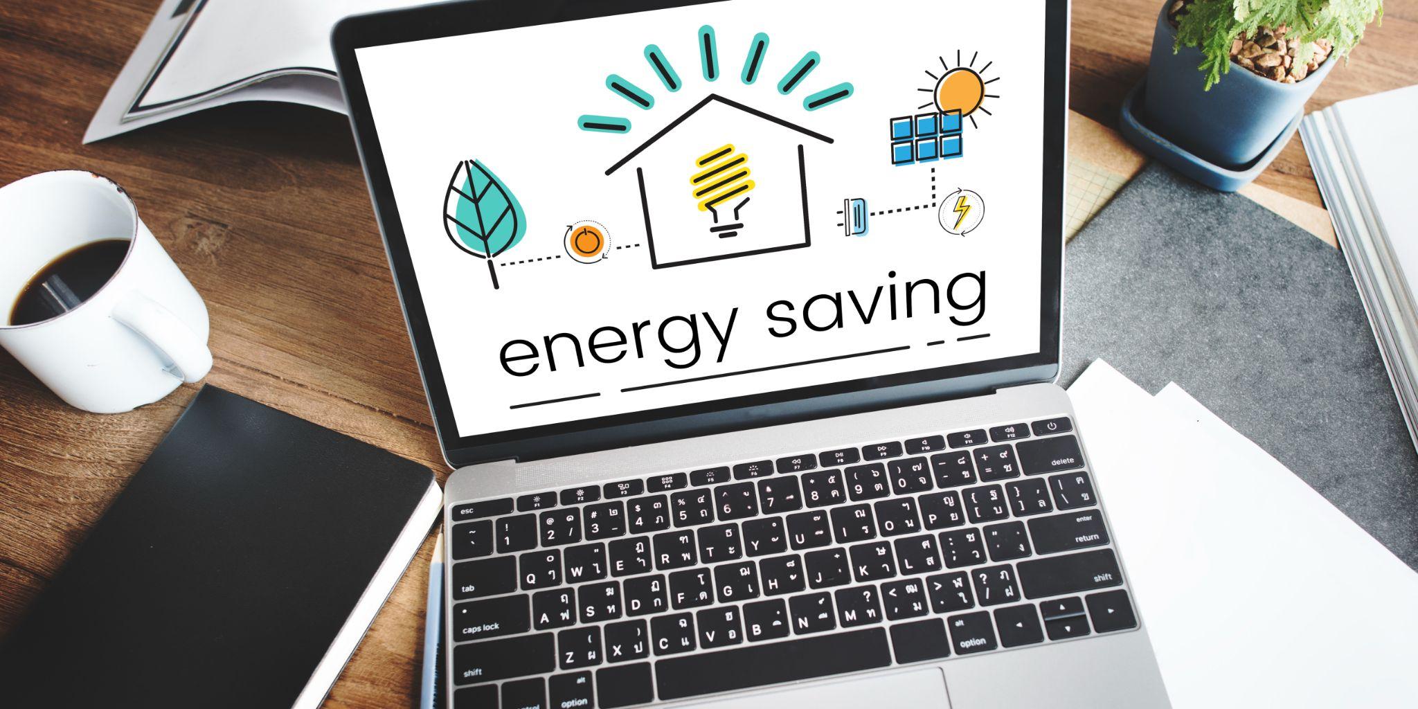 A laptop on a desk displaying an energy saving graphic beside a coffee cup and plant