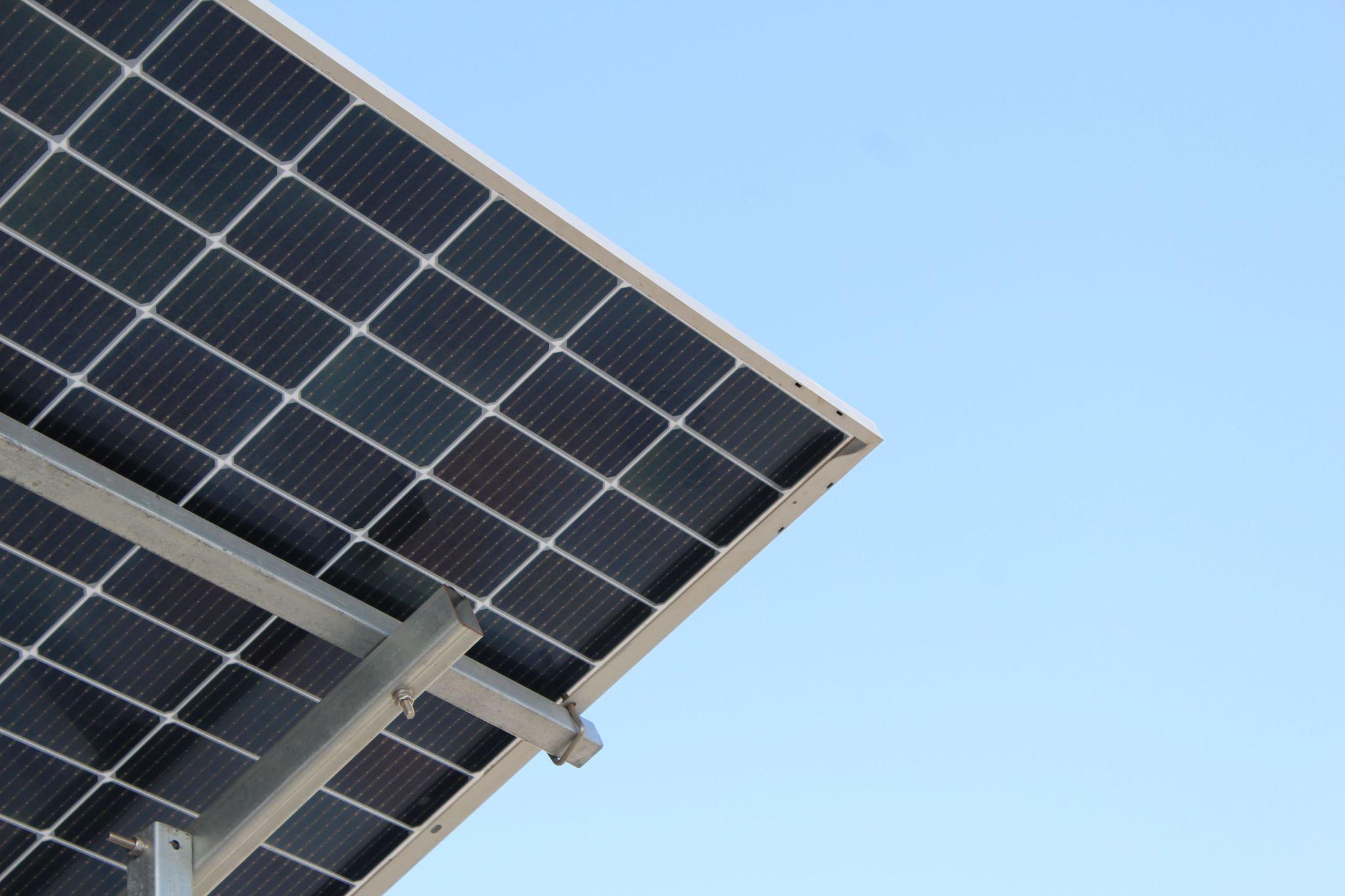 Underside of a solar panel array angled against a clear blue sky