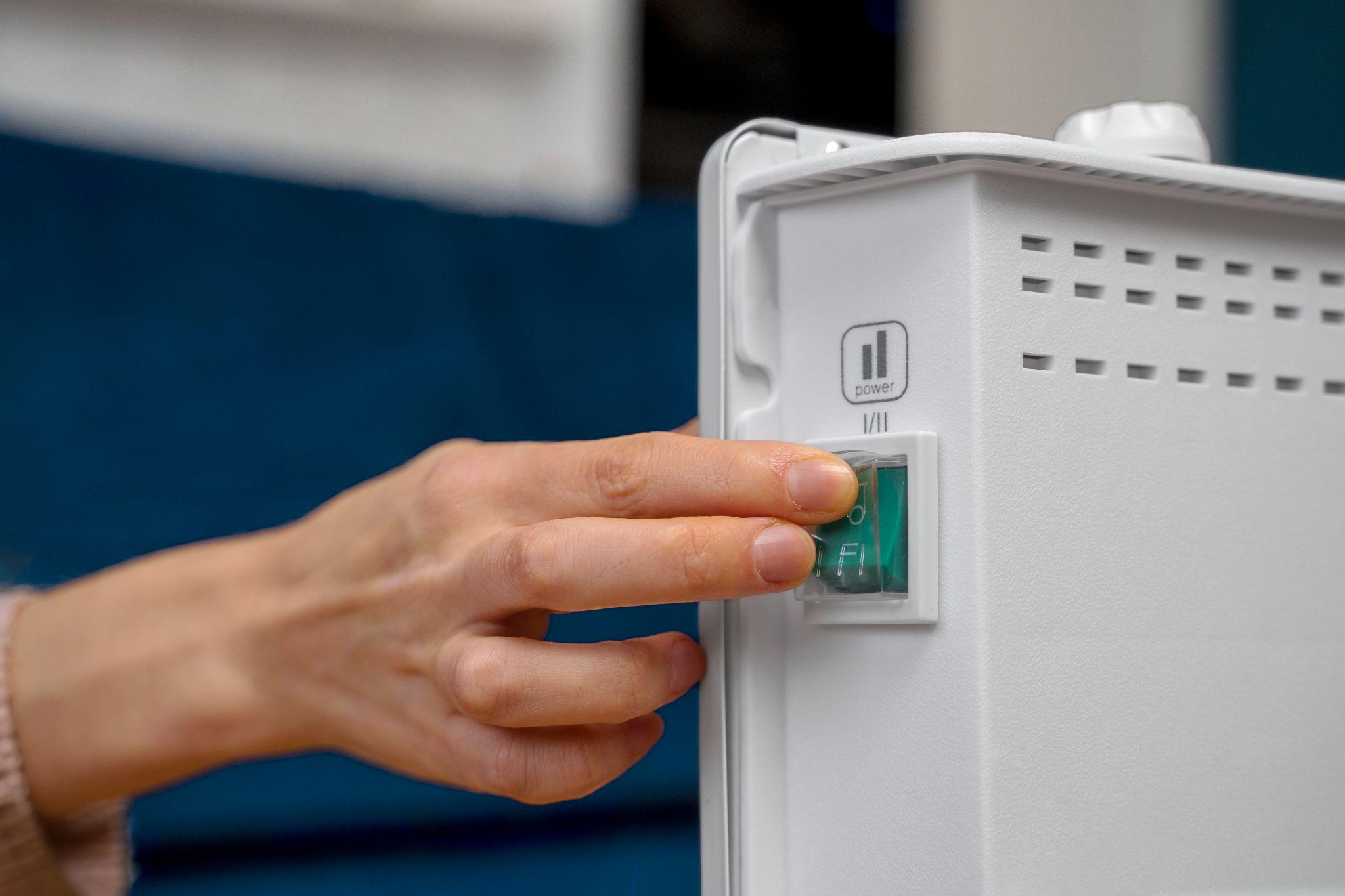 A hand switching on the power button of a white home battery unit